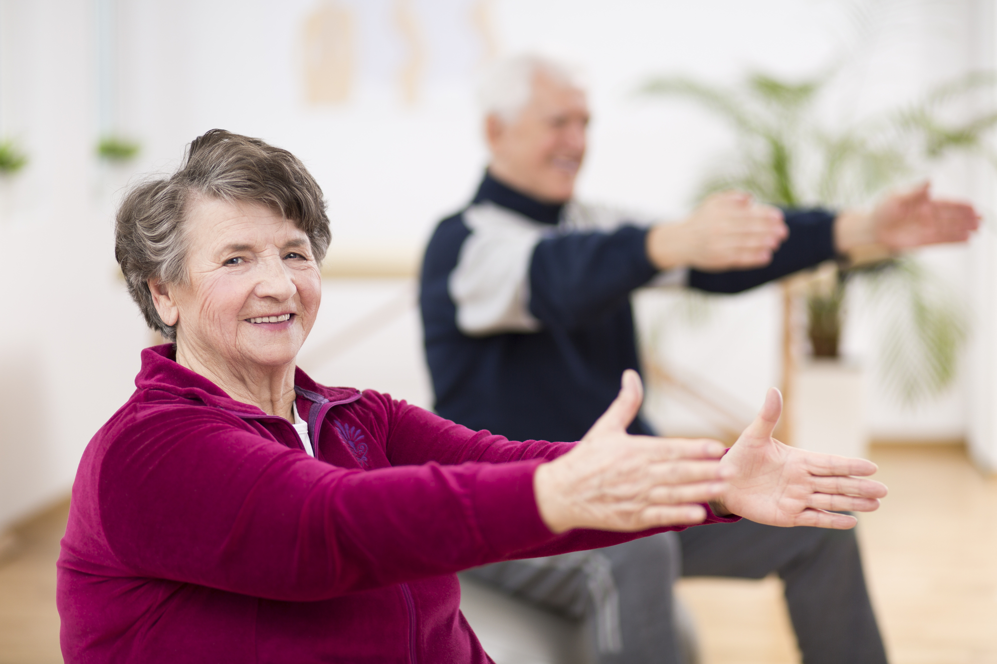 Elderly woman happily exercising with her friend during pilates for seniors